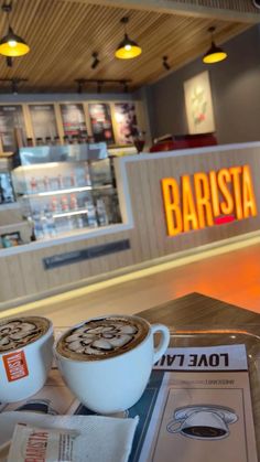 two cups of coffee sitting on top of a table in front of a sign that says barista