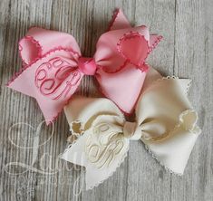 two pink and white bows with monogrammed letters on the side, one is for a baby girl