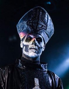 a man in skeleton makeup on stage wearing a black jacket and hat with lights behind him