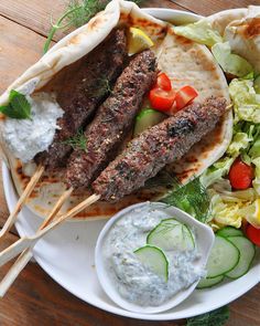 an assortment of food on a plate with skewers and sauces next to it