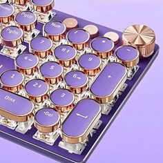 a computer keyboard with purple keys and gold knobs on the back side, in front of a purple background