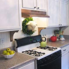 a kitchen with white cabinets and black stove top oven next to a bowl of fruit on the counter