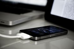 a cell phone plugged in to an external charger on a desk next to a laptop