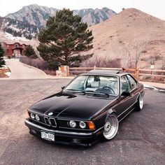 a black bmw is parked in the parking lot near some trees and mountains with snow on them