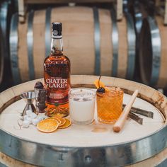 a bottle of whiskey sitting on top of a barrel next to two glasses filled with orange slices