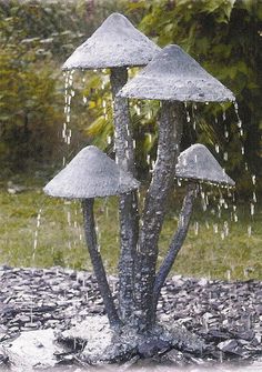 three metal mushrooms are sprinkled with water from a fountain in front of some trees