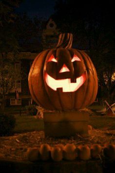 a carved pumpkin sitting in the middle of a yard at night with its eyes glowing