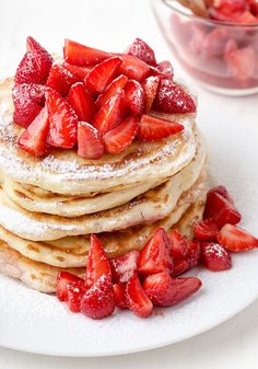 a stack of pancakes covered in powdered sugar and topped with sliced strawberries on a white plate