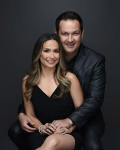 a man and woman are posing for a photo in front of a black background with their arms around each other