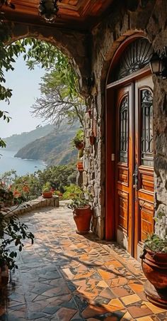 an open door to a stone building with potted plants on the outside and water in the background