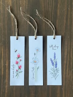 three tags with flowers are hanging from twine on a wooden table, one has writing and the other has an insect