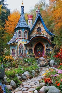 a colorful house in the woods surrounded by flowers and rocks, with a pathway leading to it