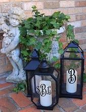 two black lanterns sitting on top of a brick floor next to a planter and statue