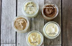 four jars filled with different types of body butter on top of a wooden table next to each other