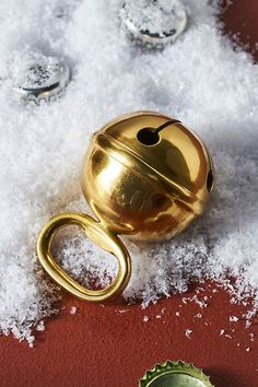 a golden bell sitting on top of snow covered ground next to a green bottle opener