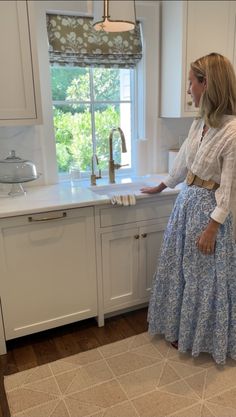 a woman is standing in the kitchen with her hands on the countertop and looking out the window