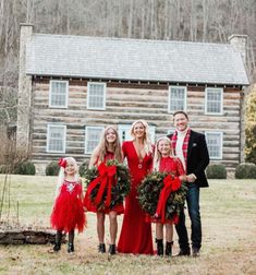 a group of people standing next to each other in front of a log cabin with wreaths