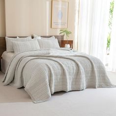 a bed with a white comforter and pillows on top of it in front of a window