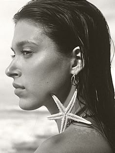 a woman with starfish earrings on her neck looking off into the distance at the ocean