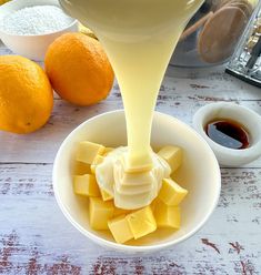 orange juice being poured into a bowl with cubes of butter in front of an orange and other ingredients