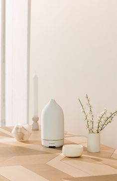 a white vase sitting on top of a wooden table next to a candle and some flowers