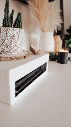 a close up of a white box on a table with plants and candles in the background