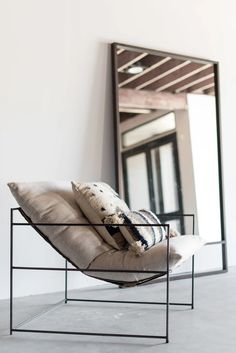 a chair that is sitting in front of a mirror with pillows on top of it