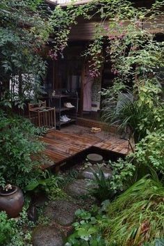 a wooden deck surrounded by greenery and potted plants in front of a house