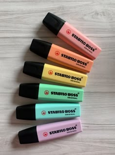 five different colored markers are lined up in a row on a white wooden surface, with the words stabio boss written below them