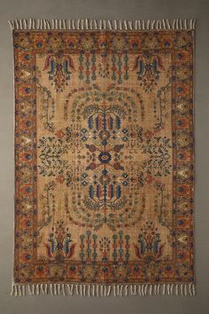 an old rug with fringes hanging on the wall in front of a gray wall