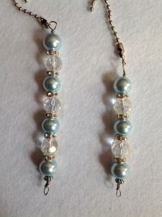 two necklaces with pearls and glass beads on a white tablecloth covered surface, one has a chain attached to it