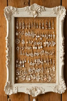 a white frame with many pairs of earrings hanging on the wall next to a wooden floor