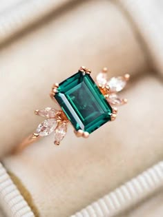 an emerald and diamond ring sitting on top of a box