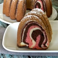 a chocolate and pink swirl cake on a white plate with another one in the background