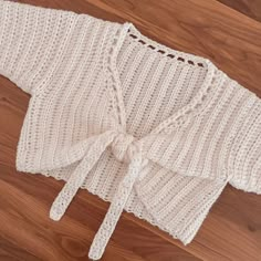 a white knitted sweater with a bow on the front and back, sitting on top of a wooden floor