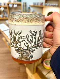 a person holding a coffee cup with a deer on it's face and antlers painted on the side