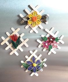 four pieces of art made out of plastic flowers on a metal surface with one flower in the center