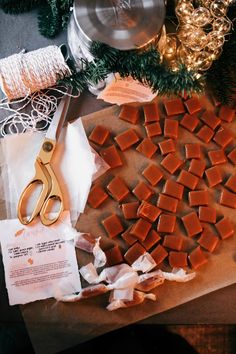 a cutting board with pieces of wax paper and scissors on it next to christmas decorations