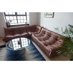 a brown leather sectional sofa sitting on top of a wooden floor next to a glass table