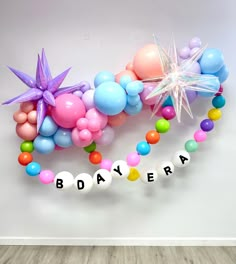 balloons and streamers with the word bdayera spelled out in white letters on a wooden floor