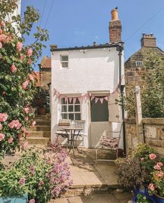 a small white house with pink flowers in the front yard and steps leading up to it