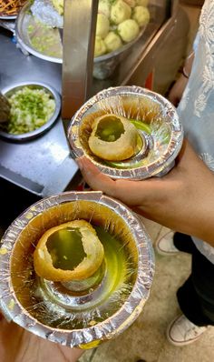 two people holding plates with food on them in front of some bowls and pans