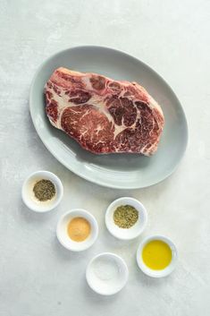 raw meat on plate with spices and seasonings in bowls, next to cut up piece of steak