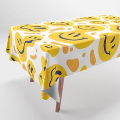 a yellow and white table cloth with smiley faces on it, sitting on top of a wooden leg