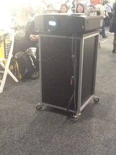 an electronic device sitting on top of a cart in the middle of a room filled with people