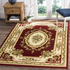 a red and white rug with an oval design on the center is in front of a window