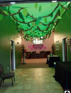 an empty room with tables and chairs in the center is decorated with green leaves hanging from the ceiling