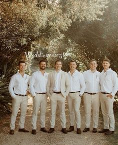 a group of men standing next to each other in front of trees and dirt ground