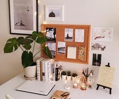 a white desk topped with lots of books next to a plant and pictures on the wall