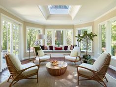 a living room filled with lots of furniture next to two large windows covered in sunlight